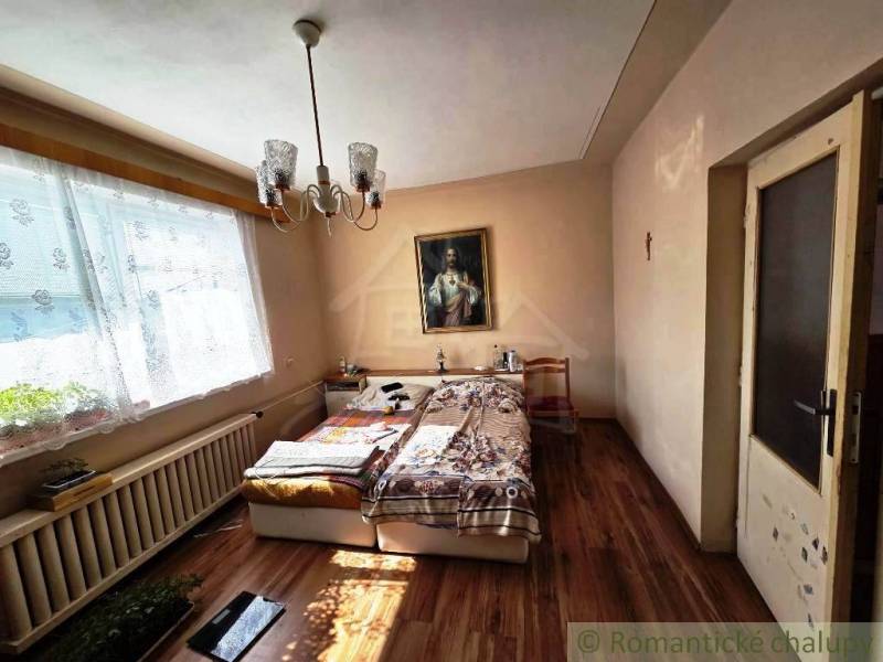 Rodinný dom s 2 bytovými jednotkami, veľkým pozemkom a hospodárskym zá - Spálňa v rodinnom dome s posteľou, lustrom, obrazom a podlahou s dreveným dekorom.