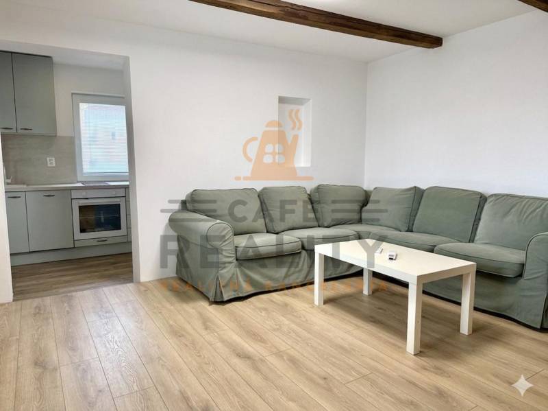 Na predaj 2 izbový murovaný domček, Bratislava, Záhorská Bystrica - Obývacia izba s rohovou pohovkou, podlahou s dreveným dekorom a kuchyňou v rodinnom dome.