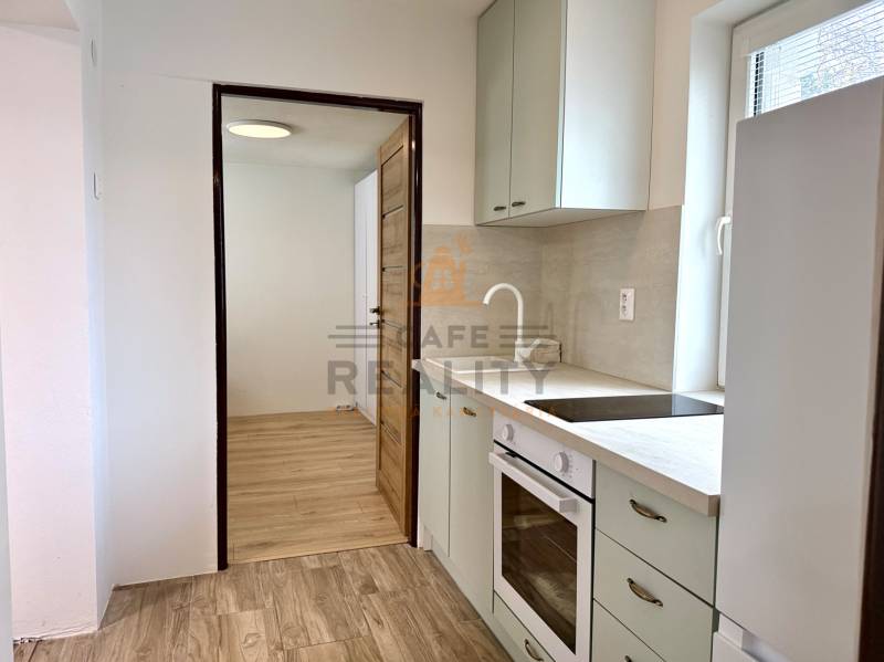 Na predaj 2 izbový murovaný domček, Bratislava, Záhorská Bystrica - Kuchyňa v 2-izbovom byte s podlahou s dreveným dekorom a bielymi skrinkami.