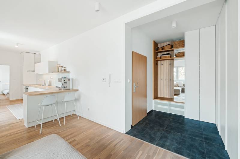 NUERA | PREDAJ 4i byt s predzáhradkou pri lese + 2x parking , BAIV - Vstupná chodba v 4-izbovom byte s podlahou s dreveným dekorom a kuchynským kútom.