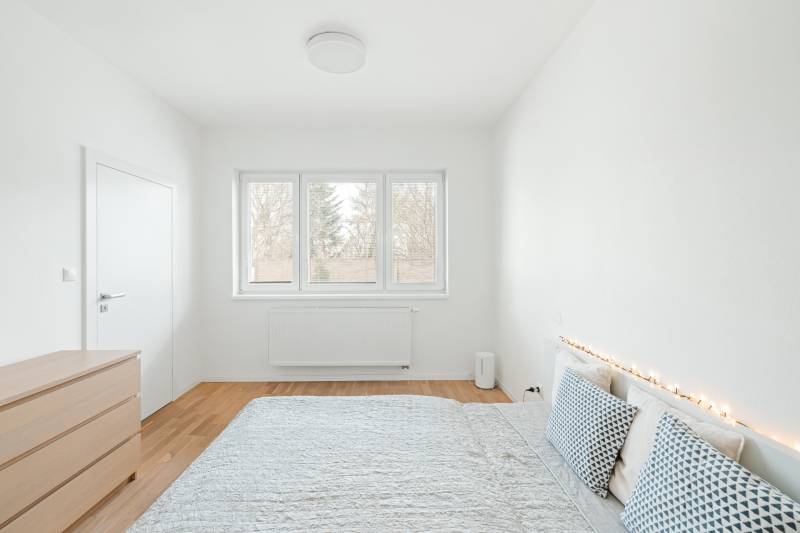 NUERA | PREDAJ 4i byt s predzáhradkou pri lese + 2x parking , BAIV - Svetlá spálňa v 4-izbovom byte s podlahou s dreveným dekorom a dekoratívnymi vankúšmi.