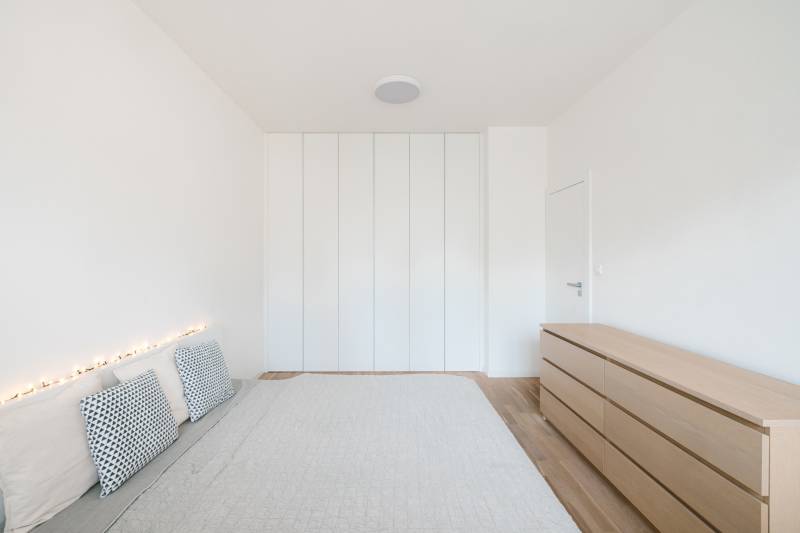 NUERA | PREDAJ 4i byt s predzáhradkou pri lese + 2x parking , BAIV - Svetlá spálňa v 4-izbovom byte s posteľou, vankúšmi a skriňou, podlaha s dreveným dekorom.