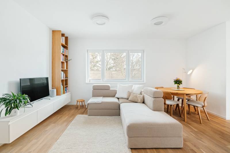 NUERA | PREDAJ 4i byt s predzáhradkou pri lese + 2x parking , BAIV - Obývacia izba so sedačkou, TV, knihovňou a jedálenským stolom, podlaha s dreveným dekorom.