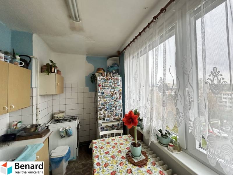 NA PREDAJ 3-IZBOVÝ BYT  S LODŽIOU, 67m2,  OKTÓBROVÁ ul,, PREŠOV - Kuchyňa 3-izbového bytu s veľkým oknom, záclonou a kvetmi na parapete.