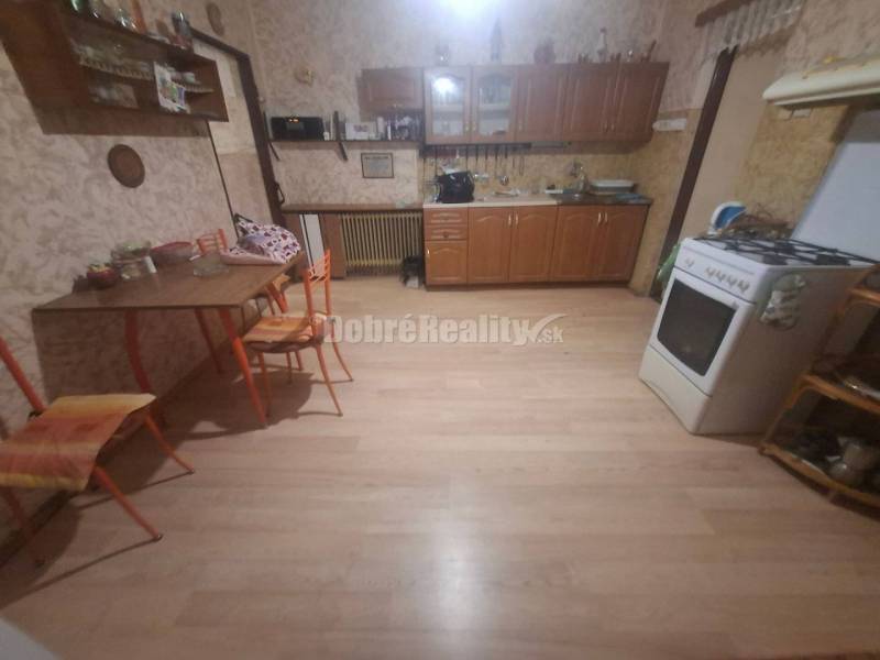 Na predaj rodinny dom v obci Iža. - Kuchyňa s plynovým sporákom, podlahou s dreveným dekorom a jedálenským stolom v rodinnom dome.