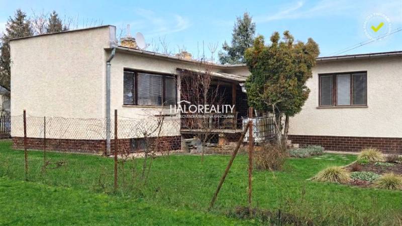 Predaj, rodinný dom Poltár - EXKLUZÍVNE HALO REALITY - Rodinný dom v Poltári obklopený trávnikom a stromami, s terasou a plotom.