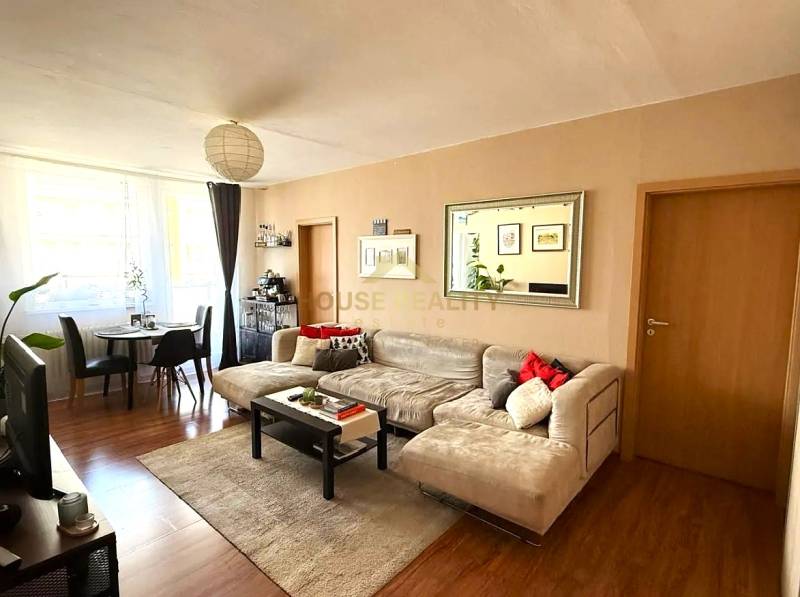 Pekný zariadený 3 izbový byt s lodžiou, Púpavová ulica, BA.Karlova Ves - Obývačka v 3-izbovom byte s podlahou s dreveným dekorom, sedačkou a jedálenským stolom.