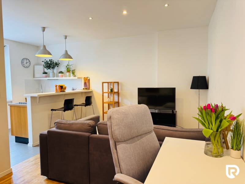 Tichý 2i byt v TOP Lokalite Nív | Trenčianska, BA - Obývacia izba s kuchyňou a podlahou s dreveným dekorom v 2-izbovom byte.