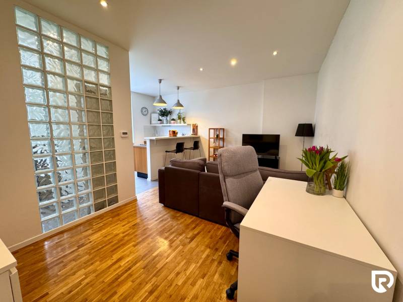 Tichý 2i byt v TOP Lokalite Nív | Trenčianska, BA - Obývacia izba v 2-izbovom byte s presklenou stenou a podlahou s dreveným dekorom.