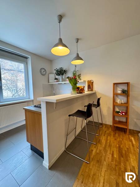 Tichý 2i byt v TOP Lokalite Nív | Trenčianska, BA - Kuchyňa v 2-izbovom byte s barovým pultom, podlahou s dreveným dekorom a závesnými lampami.
