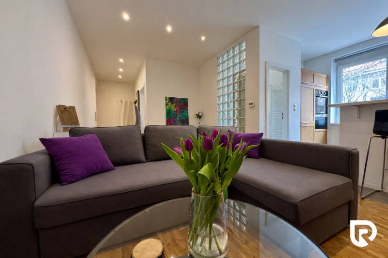 Tichý 2i byt v TOP Lokalite Nív | Trenčianska, BA - Obývačka v 2-izbovom byte s pohovkou a skleneným stolom s tulipánmi.