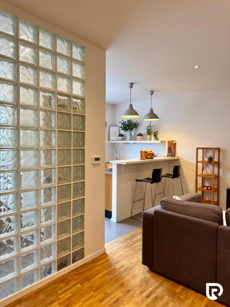 Tichý 2i byt v TOP Lokalite Nív | Trenčianska, BA - Obývačka s podlahou s dreveným dekorom a kuchynským barovým pultom v 2-izbovom byte.