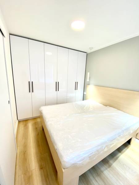 Dizajnový moderný 2 izbový byt Jurigovo nám. Bratislava IV Karlova Ves - Spálňa s manželskou posteľou, bielou skriňou a podlahou s dreveným dekorom v 2-izbovom byte.