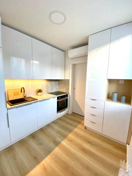 Dizajnový moderný 2 izbový byt Jurigovo nám. Bratislava IV Karlova Ves - Kuchyňa v 2-izbovom byte s bielymi skrinkami a podlahou s dreveným dekorom.