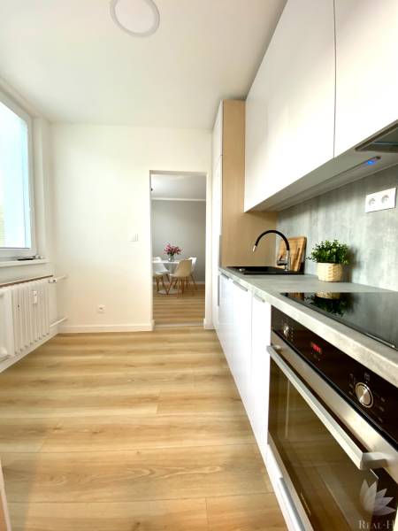 Dizajnový moderný 2 izbový byt Jurigovo nám. Bratislava IV Karlova Ves - Kuchyňa v 2-izbovom byte s bielymi skrinkami a podlahou s dreveným dekorom.