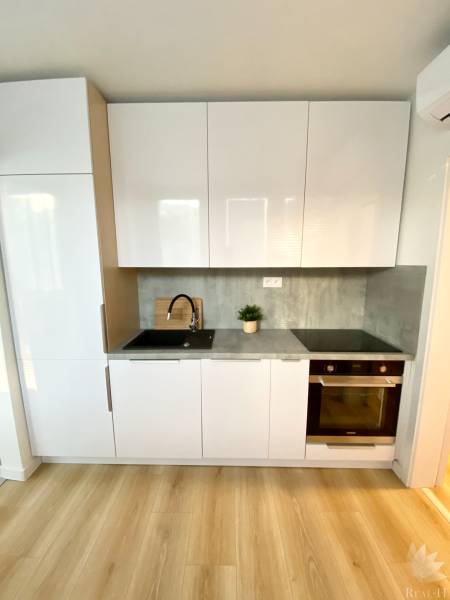 Dizajnový moderný 2 izbový byt Jurigovo nám. Bratislava IV Karlova Ves - Kuchynská linka s bielymi skriňami, sivou pracovnou doskou a podlahou s dreveným dekorom, 2-izbový byt.