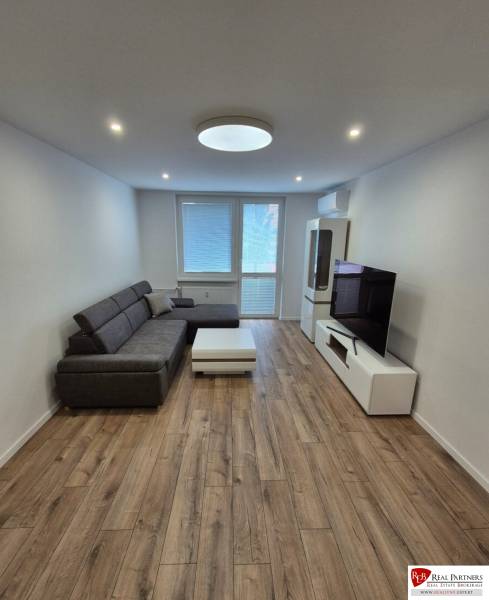 Prenájom 2-izbového bytu Bratislava II, Ružinov - Obývačka v 2-izbovom byte so sedačkou, stolíkom a televízorom na drevenej podlahe.