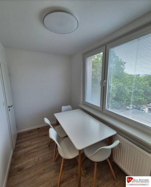 Prenájom 2-izbového bytu Bratislava II, Ružinov - Jedálenský kút v 2-izbovom byte s bielym stolom a stoličkami pri okne.