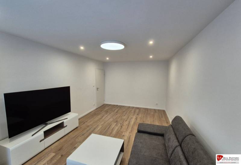 Prenájom 2-izbového bytu Bratislava II, Ružinov - Obývacia izba v 2-izbovom byte s pohovkou, televízorom a drevenou podlahou.