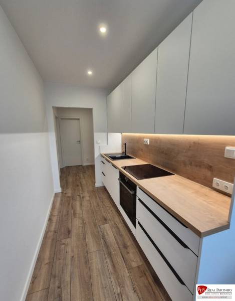 Prenájom 2-izbového bytu Bratislava II, Ružinov - Úzka kuchyňa v 2-izbovom byte s drevenou podlahou a bielymi skrinkami.