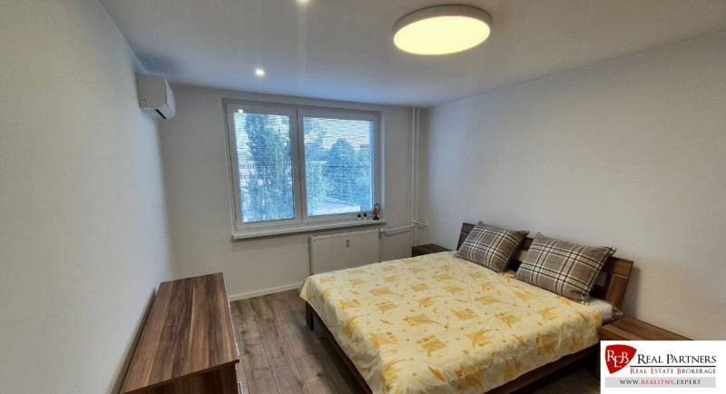 Prenájom 2-izbového bytu Bratislava II, Ružinov - Spálňa v 2-izbovom byte s pohodlnou posteľou a podlahou s dreveným dekorom.