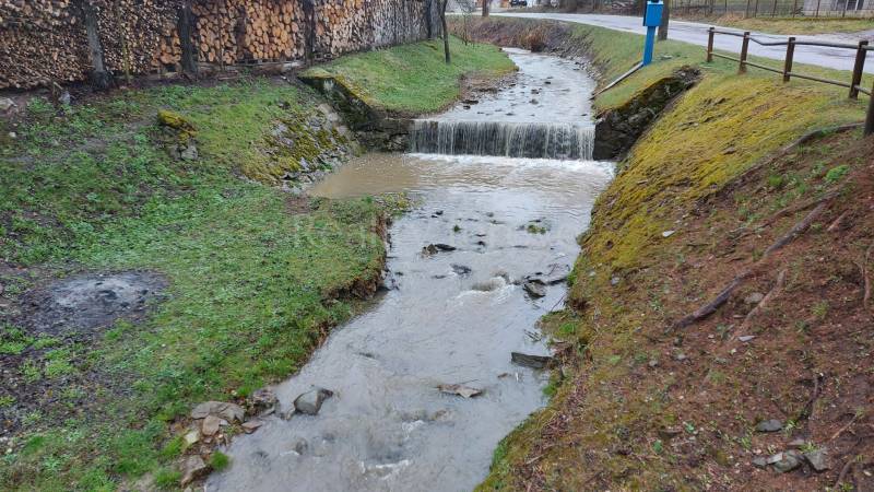 Pozemok na predaj - Vydrná - Potok tečúci cez Rekreačné pozemky v Púchove s drevom uskladneným na okraji.