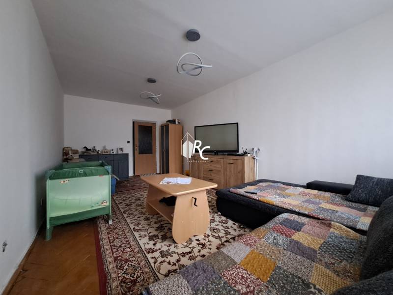 Predaj čiastočne prerobený 3 izbový byt Martin Sever - Obývacia izba v 3-izbovom byte s koberecom, pohovkou a detskou postieľkou.