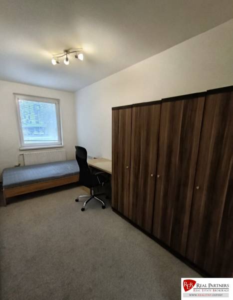 Predaj 4-izbového bytu na začiatku Petržalky Bratislava V - Izba v 4-izbovom byte s posteľou, stolom, stoličkou a skriňou na koberci.