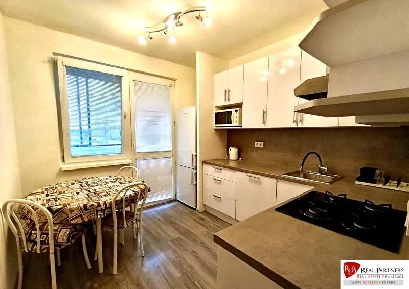 Predaj 4-izbového bytu na začiatku Petržalky Bratislava V - Kuchyňa v 4-izbovom byte s podlahou s dreveným dekorom, bielymi skrinkami a jedálenským kútom.