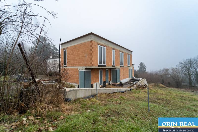 ATRAKTÍVNA MODERNÁ 5 IZB.ROZOSTAVANÁ VILA na KOLIBE - Rodinný dom na Sudovej ulici, Bratislava - Kramáre, s nedokončenou fasádou a veľkými oknami.