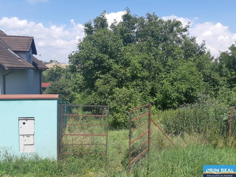 PREDAJ INVESTIČNÉHO POZEMKU V ŠENKVICIACH NA VÝSTAVBU RD - 2197 m2 - Pozemky - bývanie na Ružovej ulici v Šenkviciach, zahŕňajú bránu a zeleň.