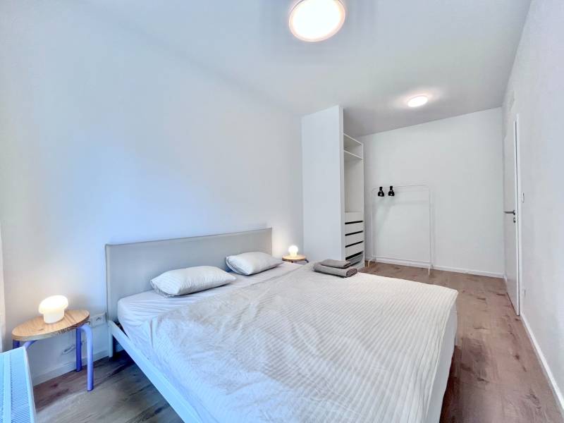 NUERA︱NOVÝ RUŽINOV - kompletne zariadený 2-izbový apartmán so záhradou - Svetlá spálňa s posteľou, nočný stolík, vešiak, podlaha s dreveným dekorom, 2-izbový byt.