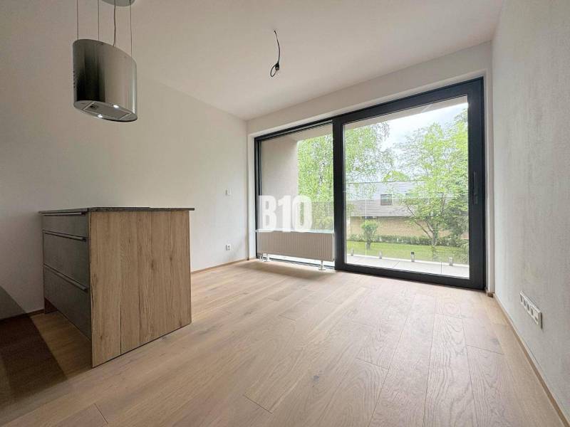 Posledný voľný APARTMÁN na kľúč - Rajecké Teplice - Interiér 2-izbového bytu s drevenou podlahou a veľkým oknom na zelený exteriér.