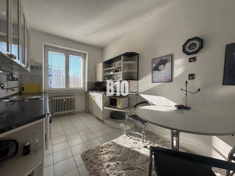 Sad na Studničkách - 2 izbový byt 60m2 - Kuchyňa v 2-izbovom byte s bielymi skrinkami, oknom a jedálenským stolom.