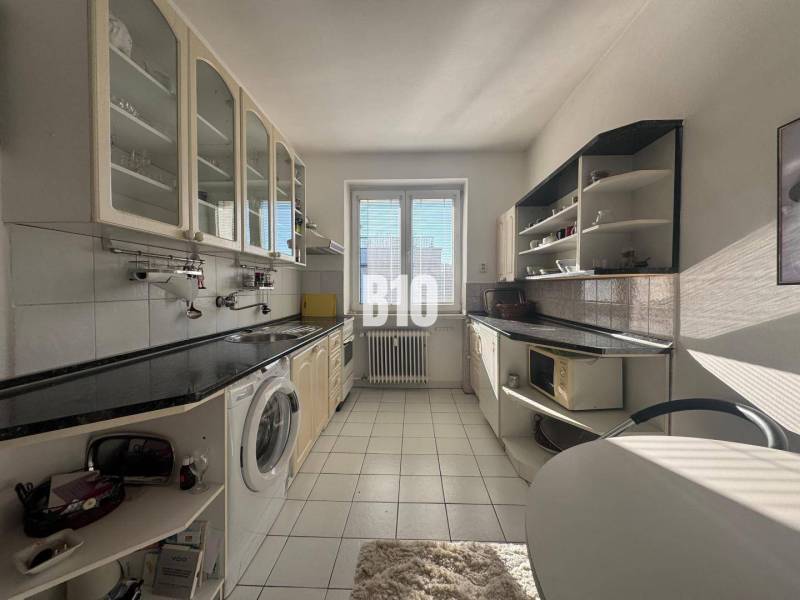 Sad na Studničkách - 2 izbový byt 60m2 - Kuchyňa v 2-izbovom byte s bielymi skrinkami a čiernou pracovnou doskou.