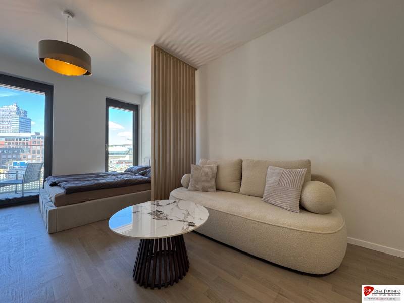 Prenájom 1-izbový byt s balkónom, METROPOLIS, Bratislava- Staré Mesto - Obývačka s pohovkou, konferenčným stolíkom a posteľou v 1-izbovom byte s podlahou s dreveným dekorom.