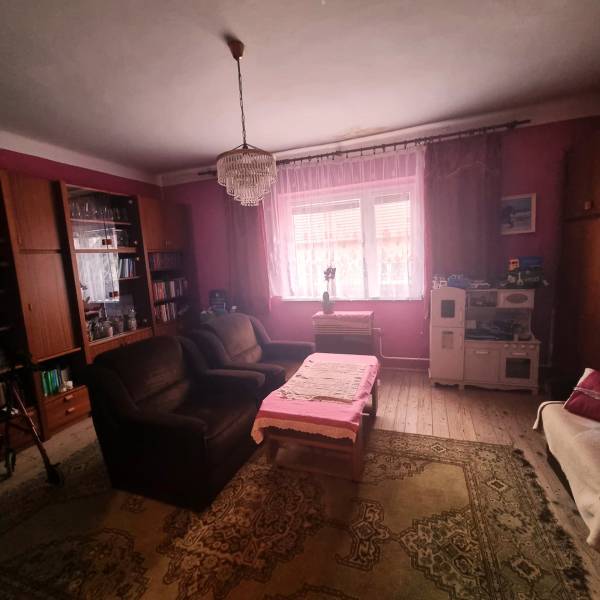 Rodinný dom na predaj - Znížená cena. - Obývacia izba rodinného domu s ružovými stenami, lustrom, pohovkou a dreveným dekorom podlahy.