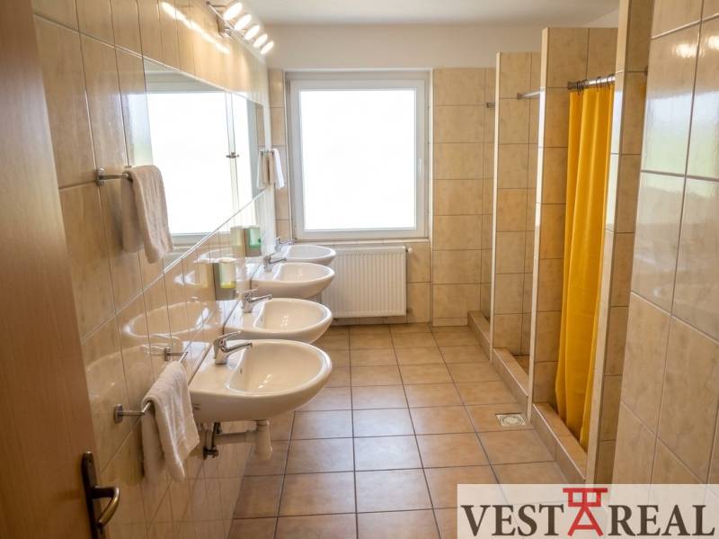 Na prenájom zrekonštruovaná ubytovňa s garážami a skladovacími kobkami - Kúpeľňa v budove ponúka umývadlá a sprchy s kachličkovou podlahou.