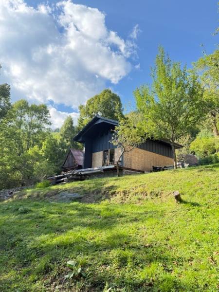 Chata pred dokončením, pozemok 770 m2, Horná Maríková - Chata v Hornej Marikovej obklopená zelenými stromami na slnečnej stráni pod modrou oblohou.