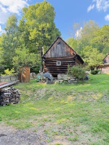 Chata pred dokončením, pozemok 770 m2, Horná Maríková - Drevená chata v Hornej Marikovej obklopená zeleňou a stohmi dreva.