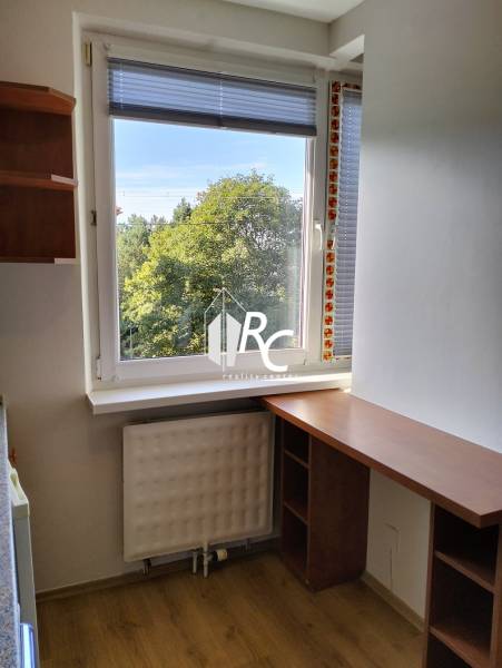 Prenájom 1-izbového bytu s energiami, Martin - Jahodníky - Malý pracovný kút so stolom, podlahou s dreveným dekorom a výhľadom na zeleň.