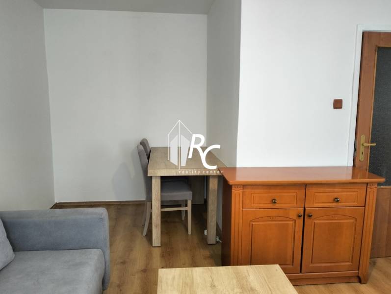 Prenájom 1-izbového bytu s energiami, Martin - Jahodníky - Interiér 1-izbového bytu so sedačkou, stolom a podlahou s dreveným dekorom.