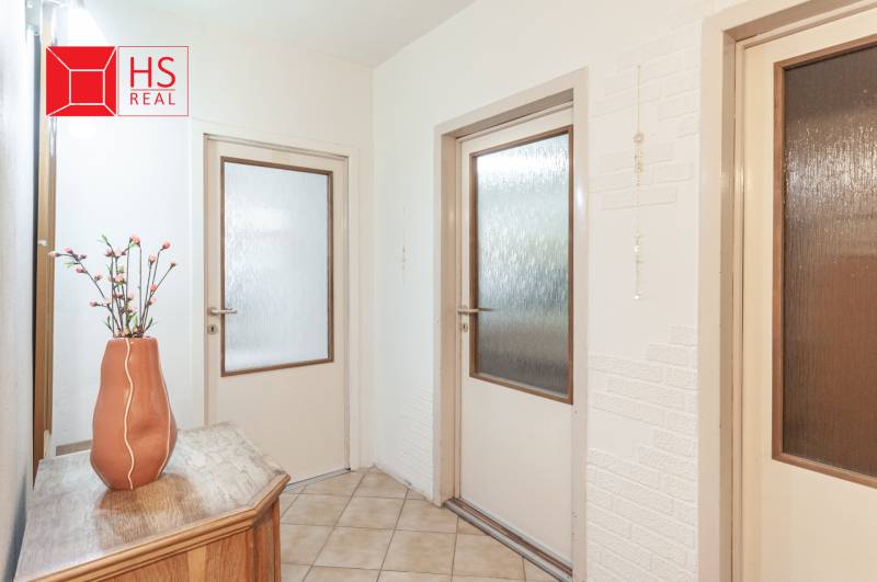 Predaj 3i bytu 84m2 - dva balkóny , Nábrežná v NZ - Chodba v 3-izbovom byte s kvetinou na drevenom stolíku a dverami s sklom.