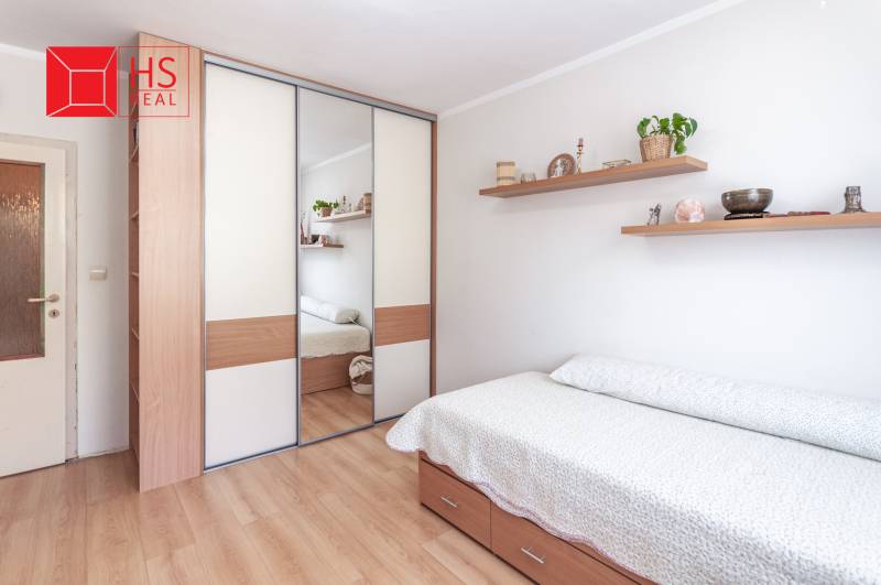 Predaj 3i bytu 84m2 - dva balkóny , Nábrežná v NZ - Spálňa v 3-izbovom byte s posteľou a zrkadlovou skriňou, podlaha s dreveným dekorom.