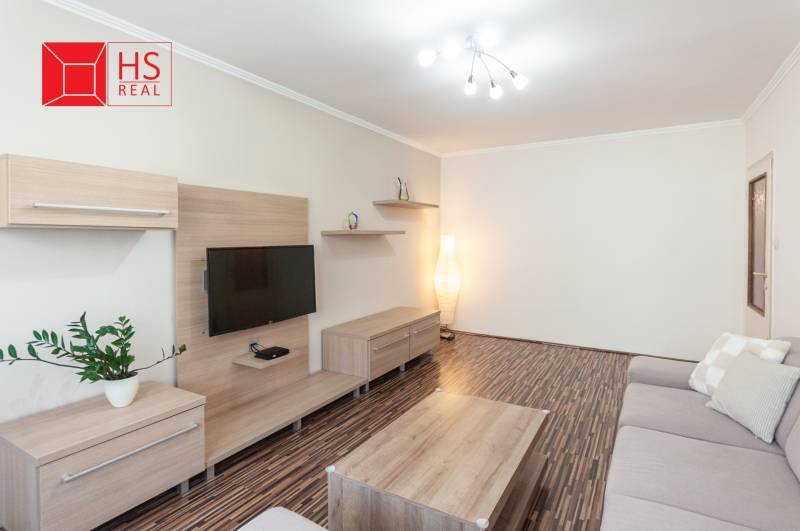 Predaj 3i bytu 84m2 - dva balkóny , Nábrežná v NZ - Obývacia izba 3-izbového bytu s podlahou s dreveným dekorom a sivou pohovkou.