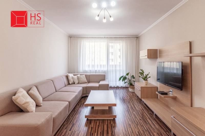 Predaj 3i bytu 84m2 - dva balkóny , Nábrežná v NZ - Obývacia izba so sedačkou, podlahou s dreveným dekorom a dekoráciami v 3-izbovom byte.