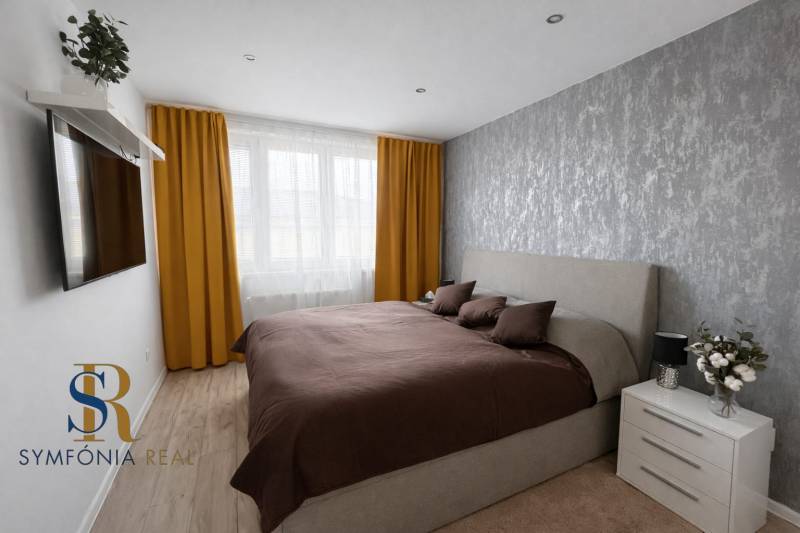 NOVINKA - Priestranných 74 m² v štýlovo zariadenom byte - Spálňa v 3-izbovom byte s podlahou s dreveným dekorom, šedou tapetou, žltými závesmi.