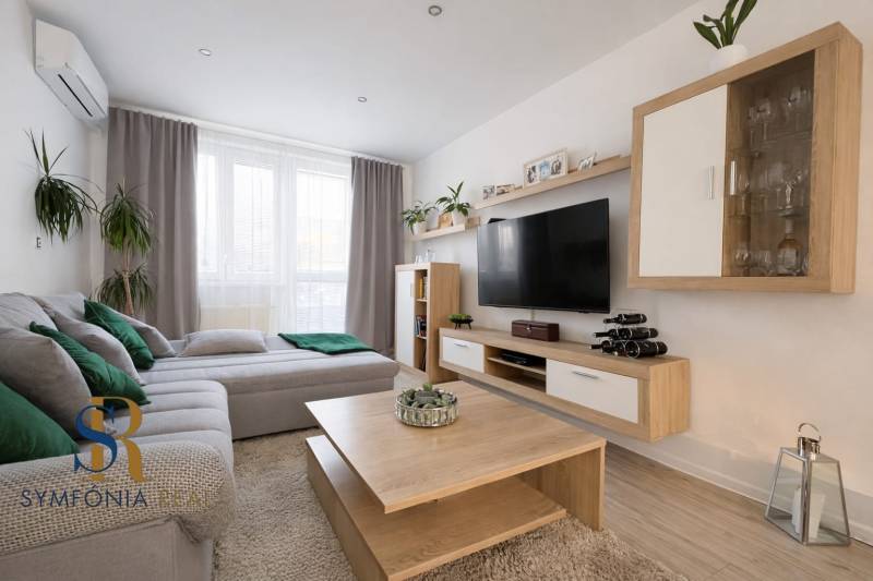 NOVINKA - Priestranných 74 m² v štýlovo zariadenom byte - Obývacia izba v 3-izbovom byte s podlahou s dreveným dekorom, pohovkou a televízorom.