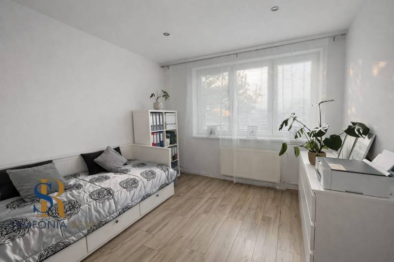 NOVINKA - Priestranných 74 m² v štýlovo zariadenom byte - Svetlá izba s posteľou, rastlinou a podlahou s dreveným dekorom v 3-izbovom byte.