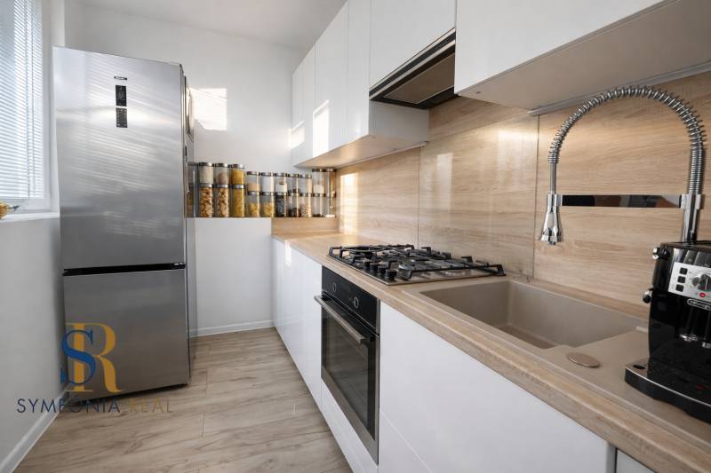 NOVINKA - Priestranných 74 m² v štýlovo zariadenom byte - Kuchyňa v 3-izbovom byte s lesklými skrinkami, nerezovou chladničkou a podlahou s dreveným dekorom.